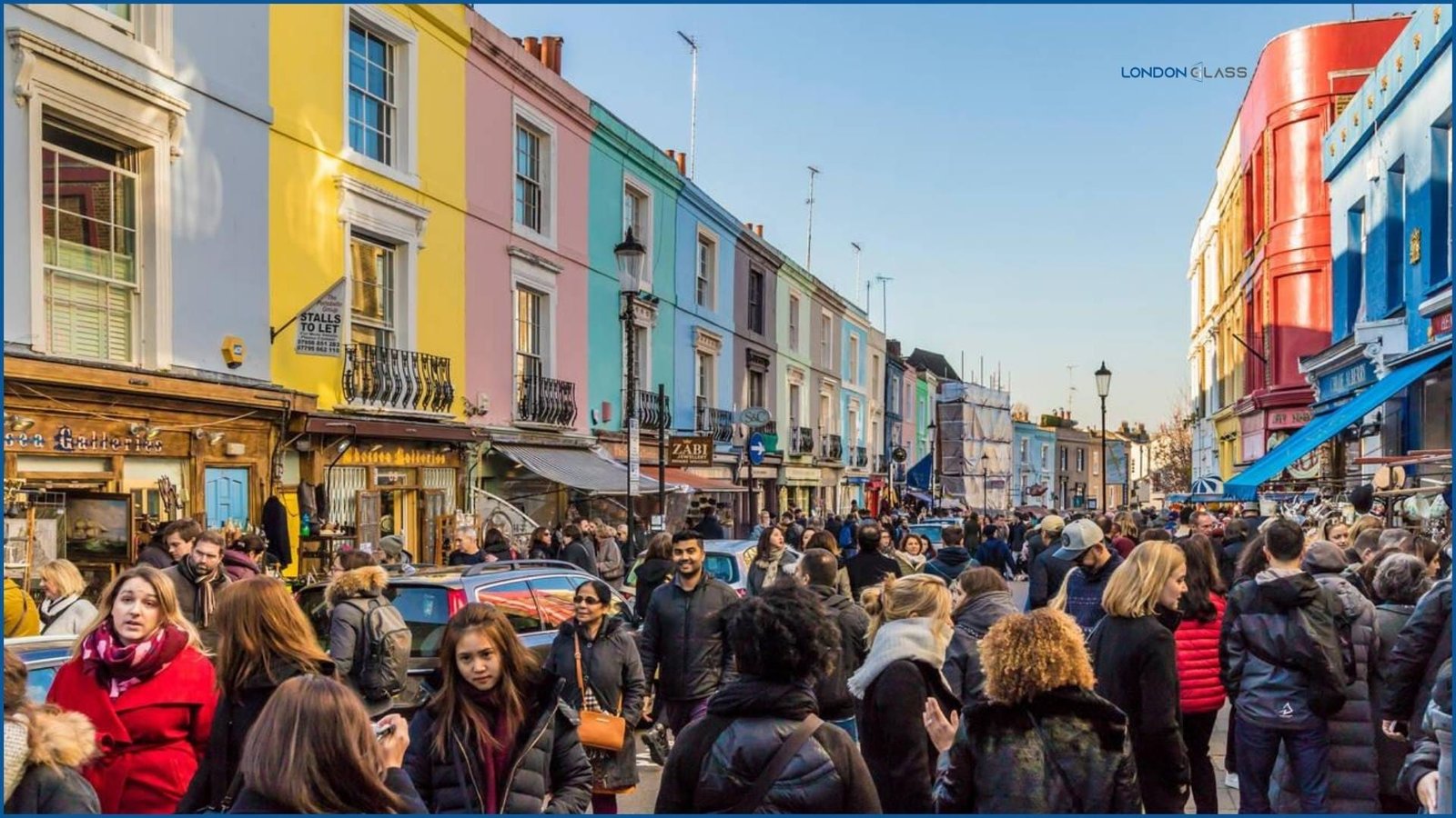 Crowded Portobello Road Market on a bright day in London, with colorful buildings lining the street.