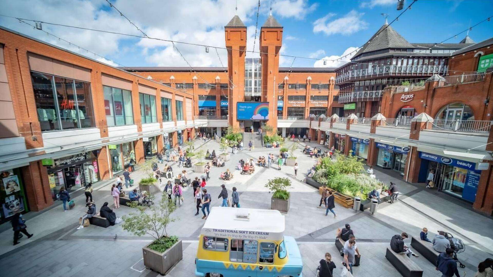 Outdoor shopping courtyard at Ealing Broadway with vibrant shops and visitors.