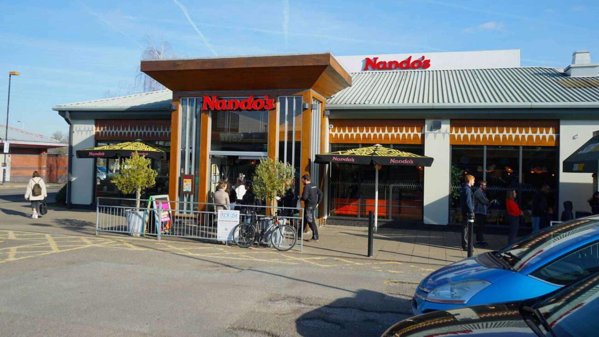 Exterior of Nando's restaurant in Park Royal, featuring outdoor seating and a modern design.