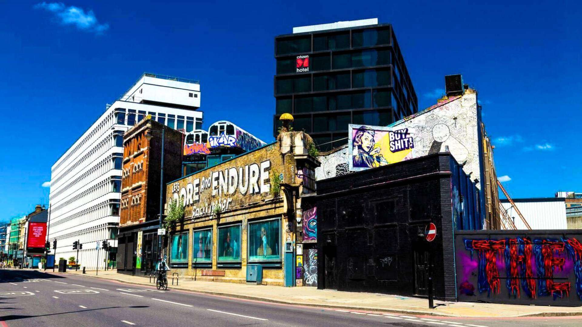 A colorful street in Shoreditch, East London, showcasing graffiti, murals, and creative urban culture under a bright blue sky.