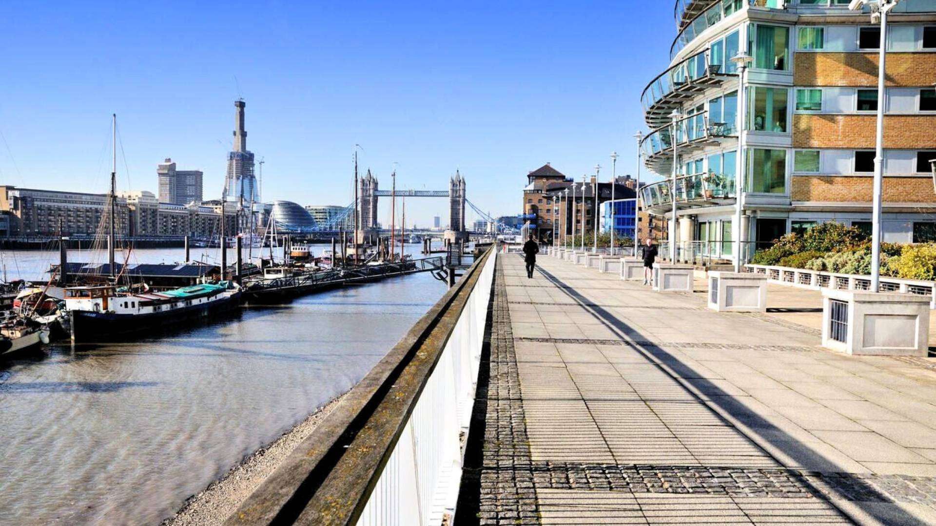 A scenic waterfront promenade in Wapping, East London, with Tower Bridge in the background and docked boats along the river.